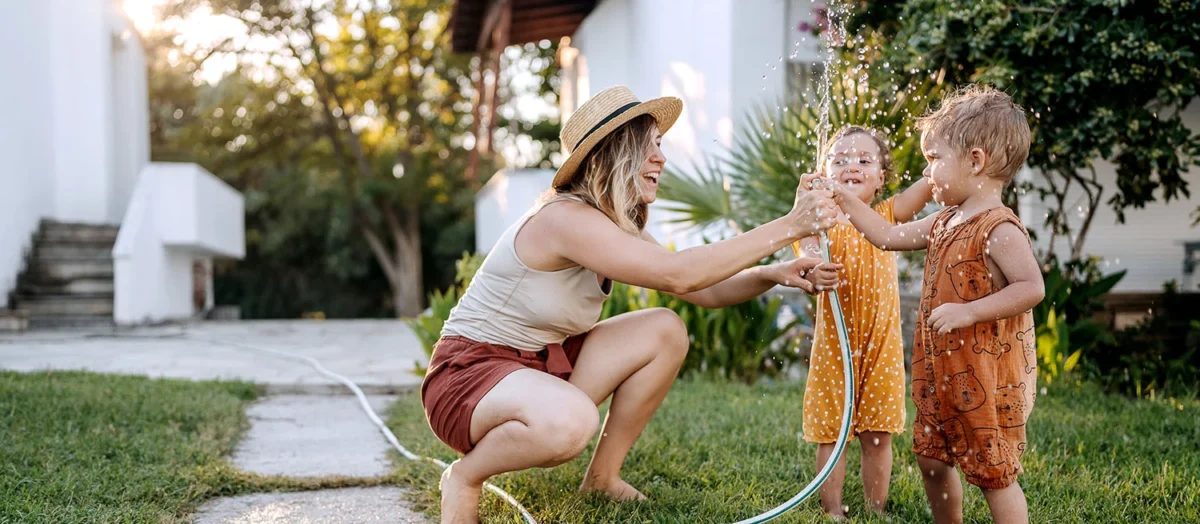 Mother playing with her two young children using a garden hose in the yard, symbolizing the everyday joy and possibilities that come from unlocking home equity.