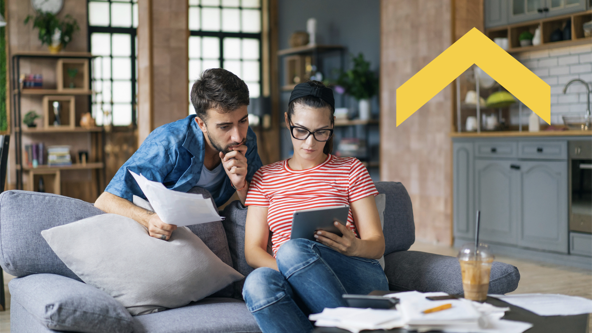 Two young homeowners sitting on a couch evaluating their budget on an iPad