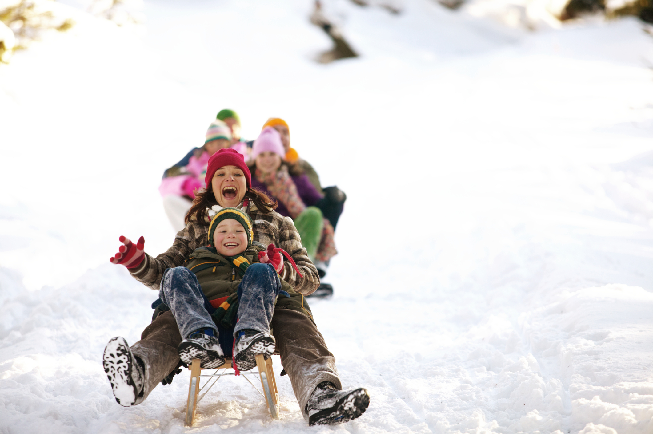 Mother and son (8-10) tobogganing in snow, family in background